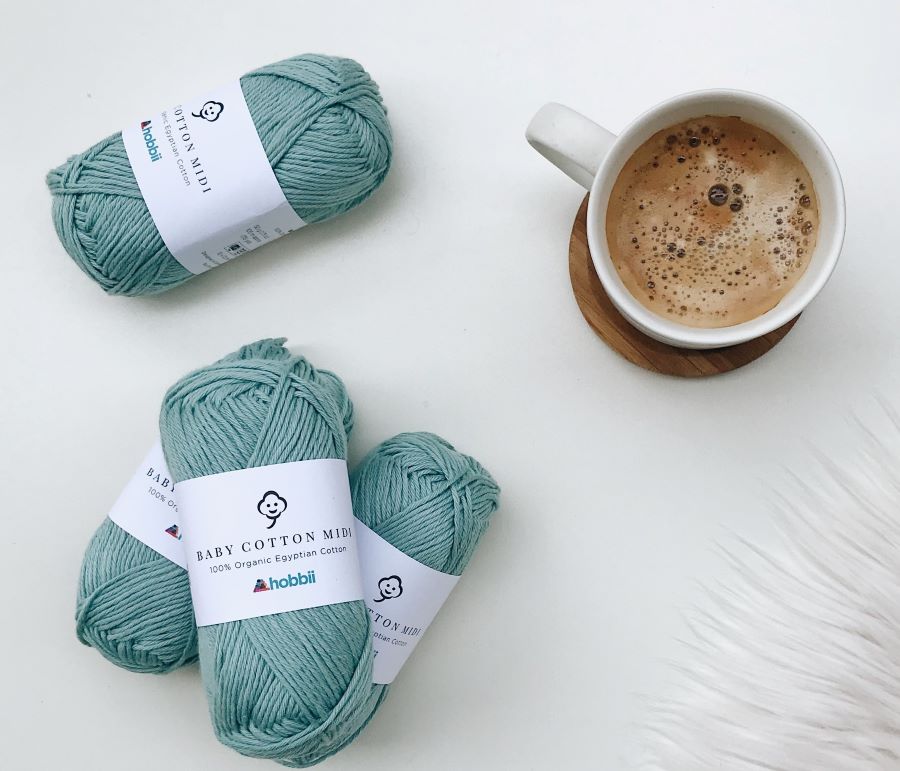 4 skeins of light blue organic cotton baby yarn, with a coffee cup